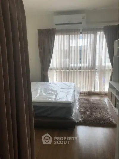Cozy bedroom with large window, sheer curtains, and air conditioning, offering a comfortable living space.