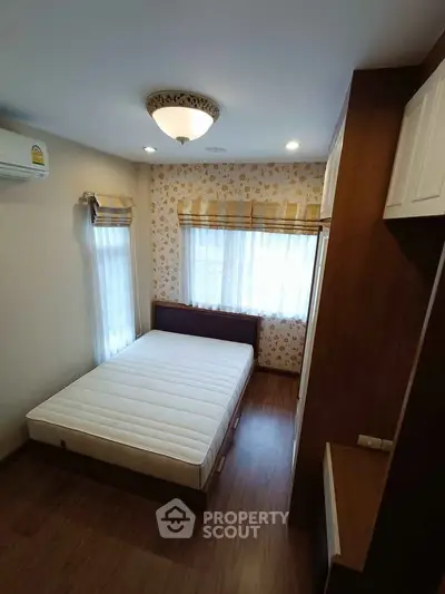 Cozy bedroom with wooden flooring and floral wallpaper, featuring a comfortable bed and ample natural light.