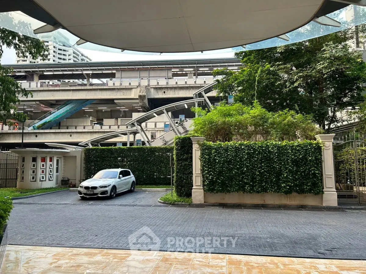 Modern urban entrance with sleek car and lush greenery, near public transit.