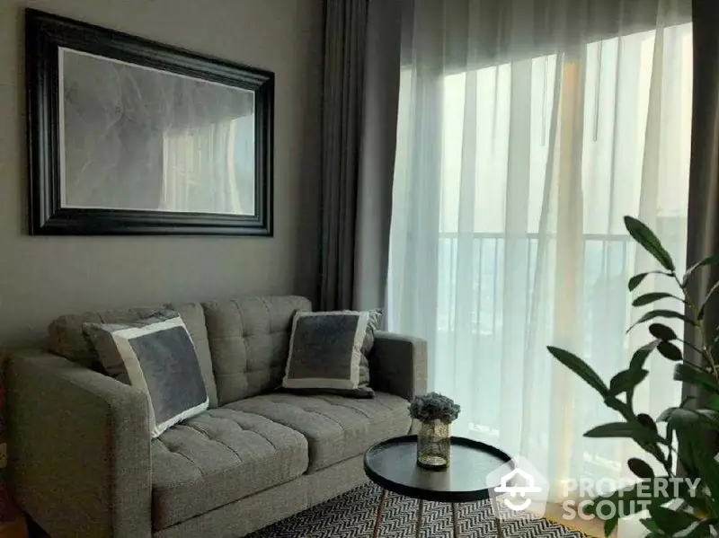 Elegant living room with plush grey sofa, chic black coffee table, and sheer curtains allowing natural light to enhance the cozy ambiance.