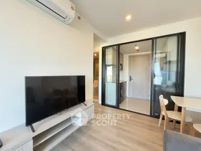Modern living room with sleek TV setup and glass partition, featuring light wood flooring and contemporary furniture.