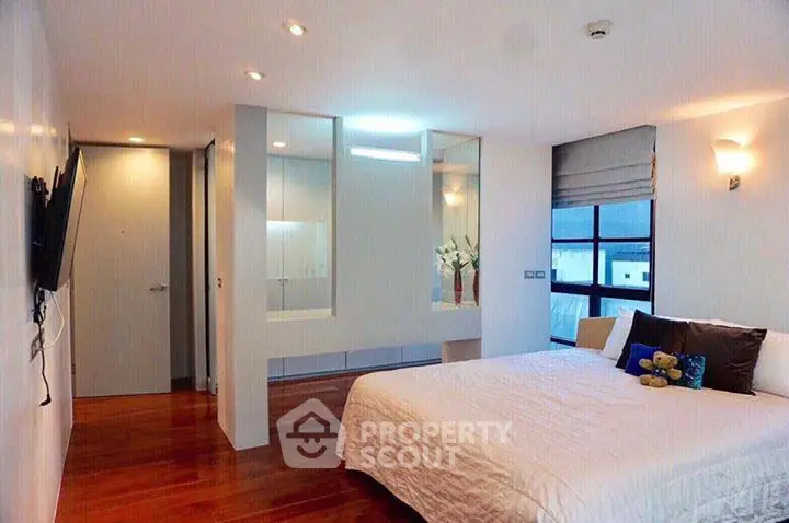 Spacious modern bedroom with wooden flooring and large windows for natural light.