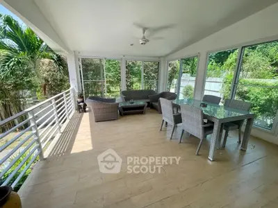 Spacious sunlit balcony with modern wicker furniture and lush garden views.