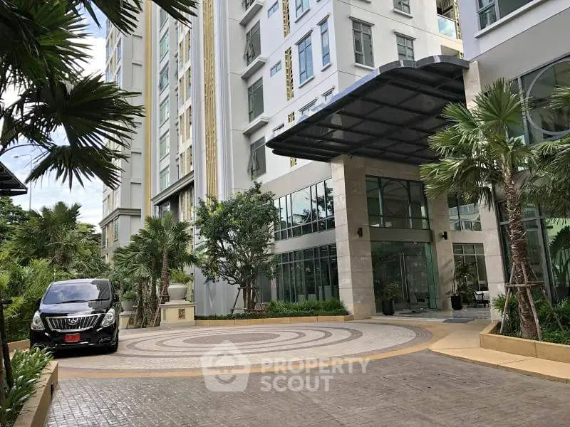 Luxurious modern building entrance with lush greenery and circular driveway.