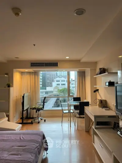 Modern studio apartment with large windows and city view, featuring a cozy living area and workspace.