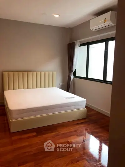 Spacious bedroom with wooden flooring and large window for natural light.