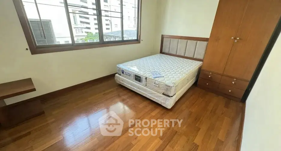 Spacious bedroom with wooden flooring and large window in modern apartment.