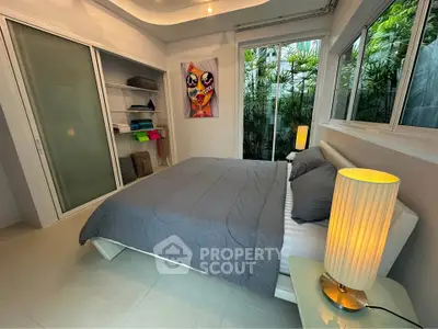 Modern bedroom with large windows and garden view, featuring sleek furniture and contemporary decor.