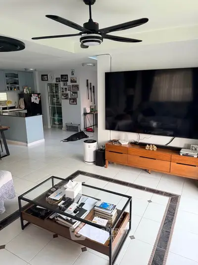 Spacious living room with modern decor and large TV, open layout to kitchen, ideal for family gatherings.