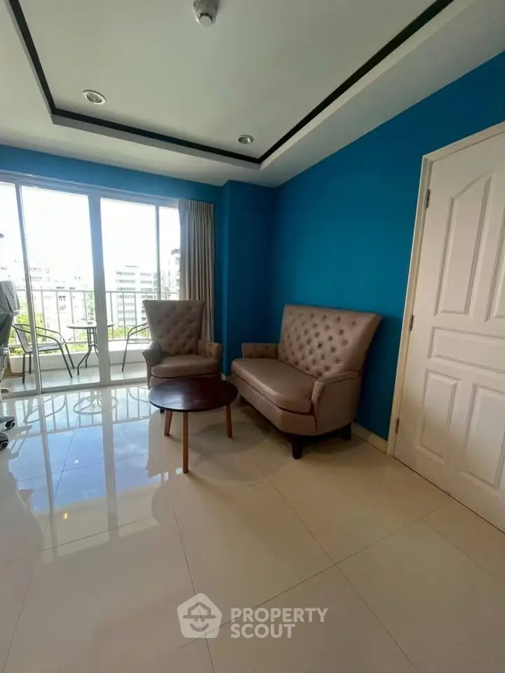 Bright living room with blue accent wall and modern furniture, featuring large windows and glossy tiled floor.