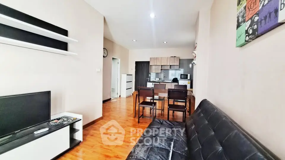 Modern living room with open kitchen, sleek furniture, and wooden flooring.