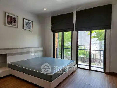 Modern bedroom with large windows and balcony access, featuring sleek design and natural light.