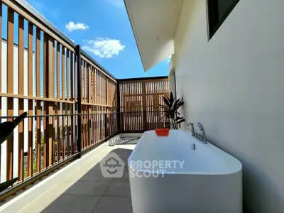 Luxurious outdoor bathtub on a private balcony with modern wooden slat design and clear blue sky view.