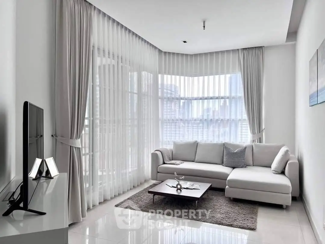 Spacious and modern living room with abundant natural light, featuring a large L-shaped sofa, sleek flat-screen TV, and elegant sheer curtains.