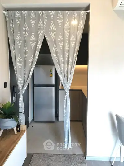 Cozy kitchen with modern fridge and stylish curtain divider in compact apartment.