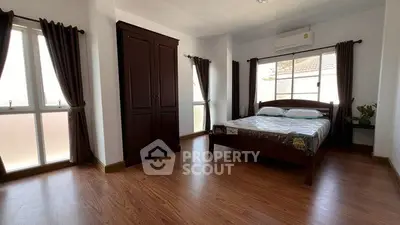 Spacious bedroom with wooden flooring and large windows for natural light.