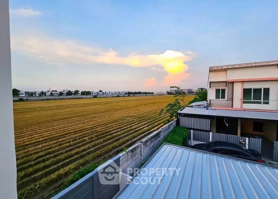 Stunning rural view from a modern home balcony overlooking expansive fields at sunset.