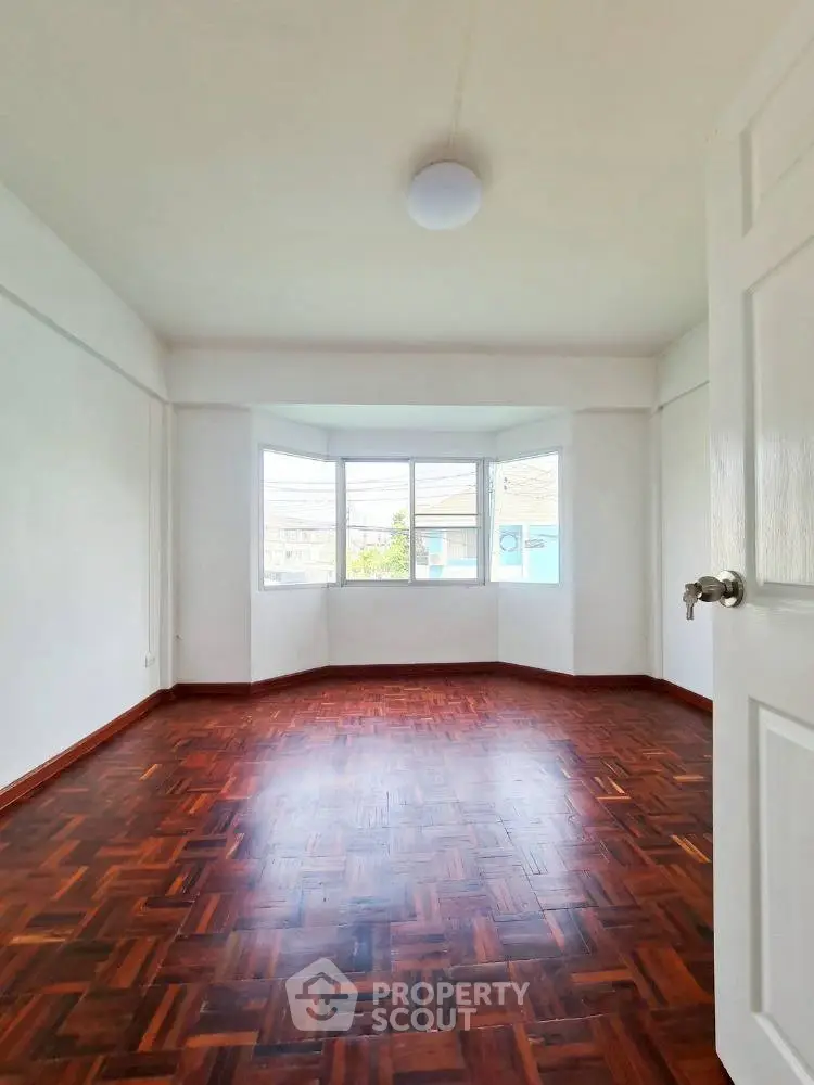 Spacious empty room with large window and wooden flooring, perfect for customization.
