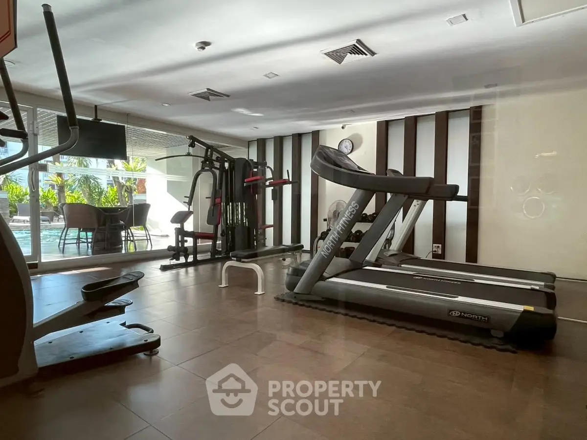Modern gym with treadmills and exercise equipment overlooking a pool area.