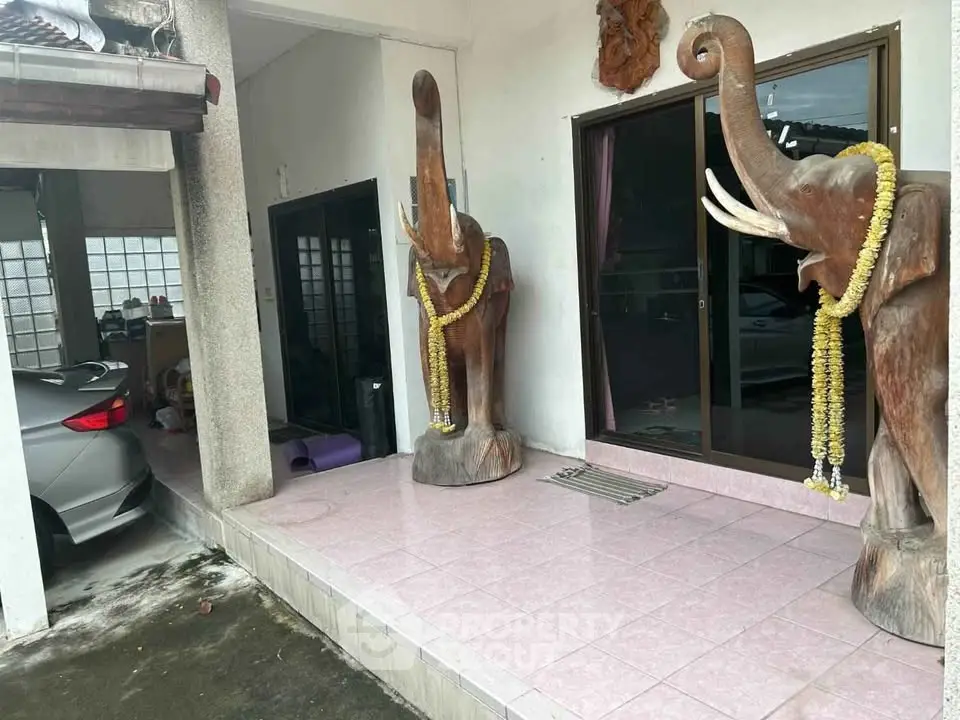 Charming home entrance with unique elephant statues and covered parking area.