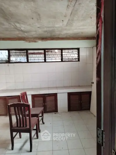 Spacious room with tiled walls and floor, featuring wooden chairs and storage cabinets.