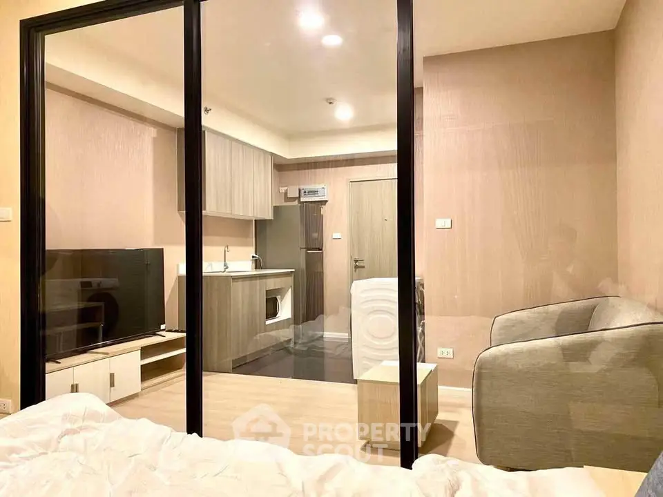 Modern studio apartment with glass partition, cozy living area, and compact kitchen.