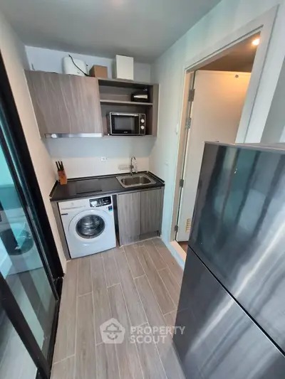Modern compact kitchen with washing machine and stainless steel fridge in a stylish apartment.