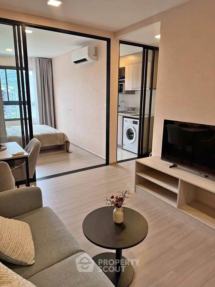 Modern open-plan living room with kitchen and bedroom, featuring sleek furniture and natural light.