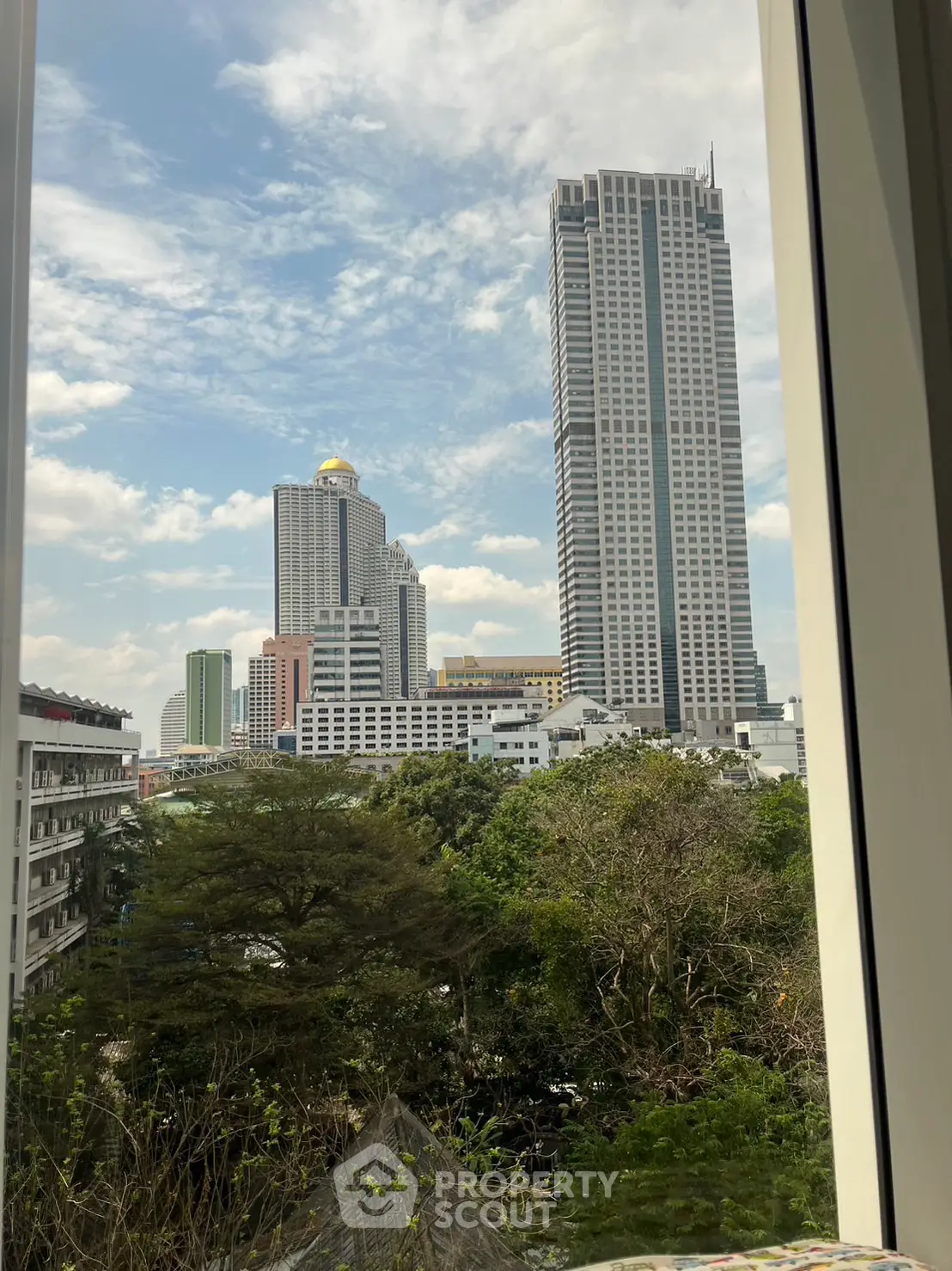 Stunning cityscape view from a window with high-rise buildings and lush greenery.
