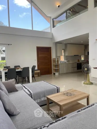 Spacious modern living room with high ceilings and open kitchen layout, featuring elegant furniture and large windows.
