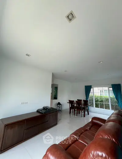 Spacious living room with leather sofa and dining area, featuring large windows and modern decor.