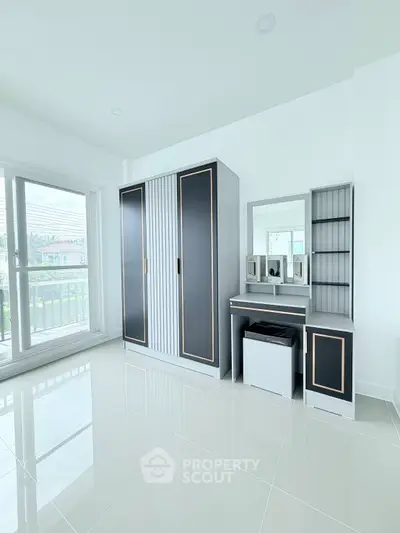 Modern bedroom with sleek wardrobe and vanity set, featuring large windows for natural light.