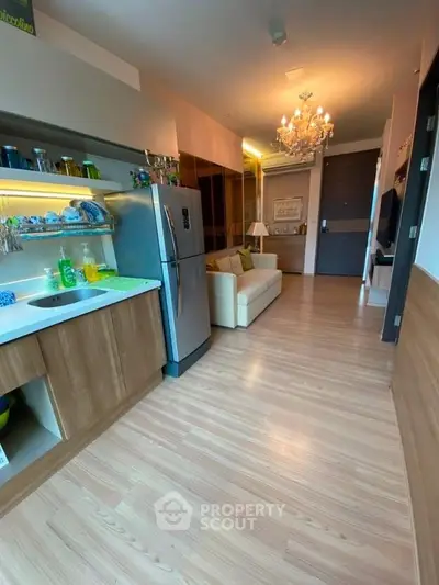 Modern open-layout kitchen and living room with elegant chandelier and wooden flooring.