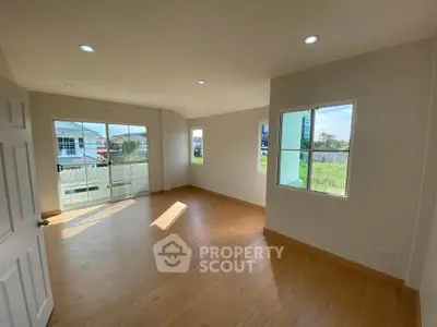 Spacious sunlit room with wooden flooring and large windows offering scenic views.
