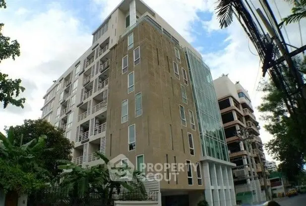 Modern apartment building with glass facade and balconies in urban setting.
