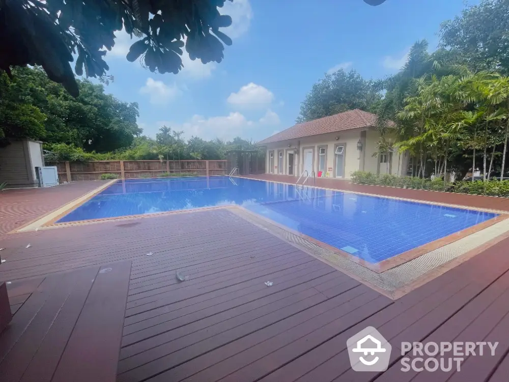 Luxurious outdoor pool area with wooden deck and lush greenery, perfect for relaxation and leisure.