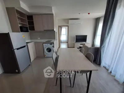 Modern open-plan kitchen and living area with dining table, washing machine, and natural light.