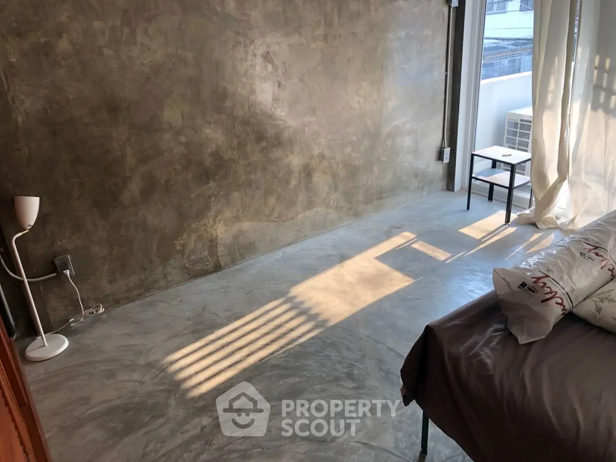 Minimalist bedroom with concrete walls and floor, natural light streaming in.