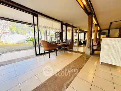 Spacious living area with large windows and outdoor view, featuring elegant wicker furniture and tiled flooring.