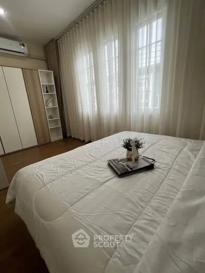 Cozy bedroom with elegant decor, featuring a large bed, stylish wardrobe, and natural light through sheer curtains.