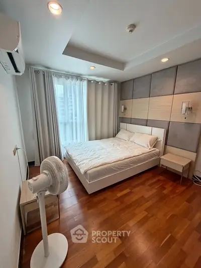Modern bedroom with wooden flooring, stylish wall paneling, and natural light from large window.