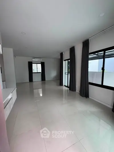 Spacious modern living room with large windows and sleek tile flooring, perfect for natural light and open living.