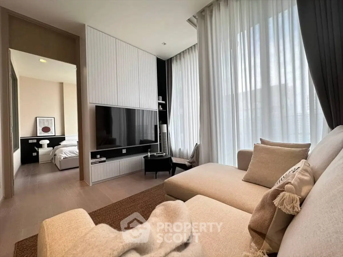 Modern living room with cozy sectional sofa and large TV, leading to a stylish bedroom.