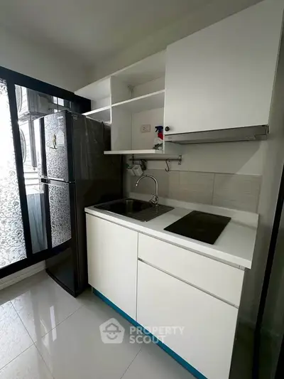 Modern kitchen with sleek white cabinets, induction cooktop, and large fridge near a window with decorative glass.