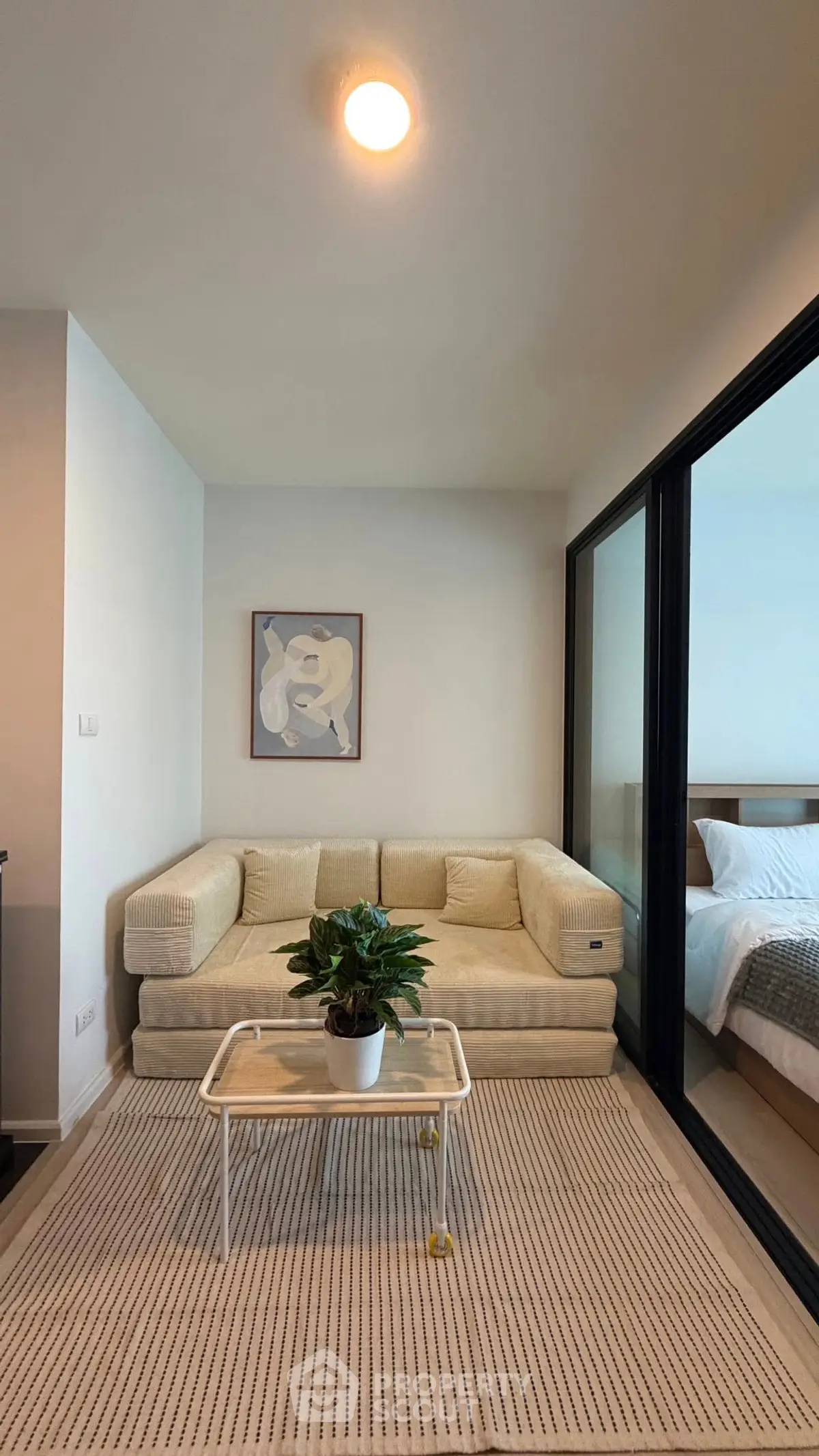 Cozy living room with beige sofa, modern decor, and sliding glass doors leading to a bedroom.