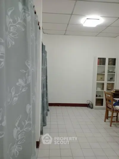 Spacious room with tiled floor, floral curtains, and a bookshelf, ideal for study or office use.