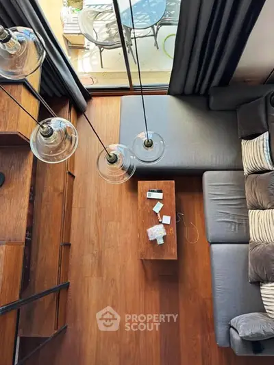 Modern living room with stylish lighting and wooden flooring, featuring a cozy gray sofa and a view of the balcony.