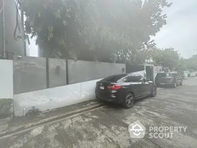 Modern residential street view with parked cars and lush greenery.