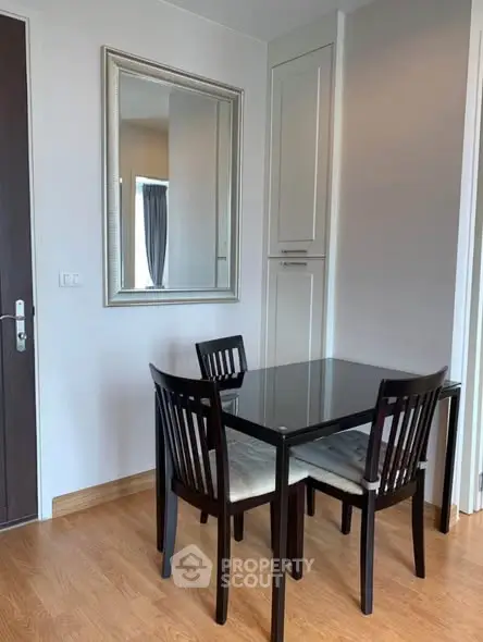 Modern dining area with sleek black table and chairs, wooden flooring, and elegant wall mirror.