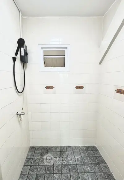Minimalist bathroom with tiled walls and floor, featuring a shower head and small window.